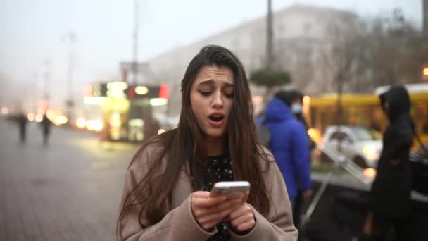 Mladá žena kráčí po ulici a psaní ve svém mobilním telefonu. — Stock video