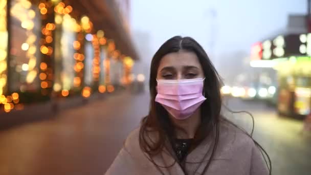 Mladá žena v ochranné masce a kabátu kráčí po ulici — Stock video