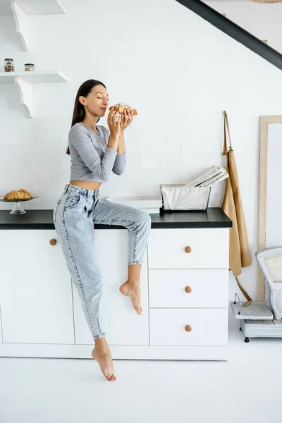 รูปภาพของผู้หญิงที่มีความสุข กินครัวซองต์อร่อยที่บ้าน . — ภาพถ่ายสต็อก