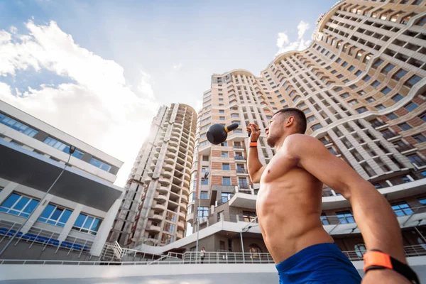 Sportive guy training with kettlebell on the background of a tall building. Royalty Free Stock Images