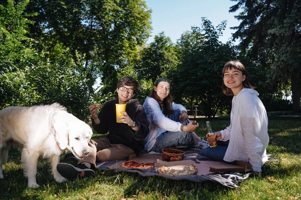 Companhia de belos jovens e cão tendo um almoço ao ar livre. — Fotografia de Stock