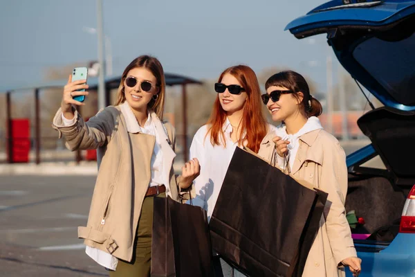 Mladé ženy v autě s nákupními taškami. Holky berou selfie — Stock fotografie