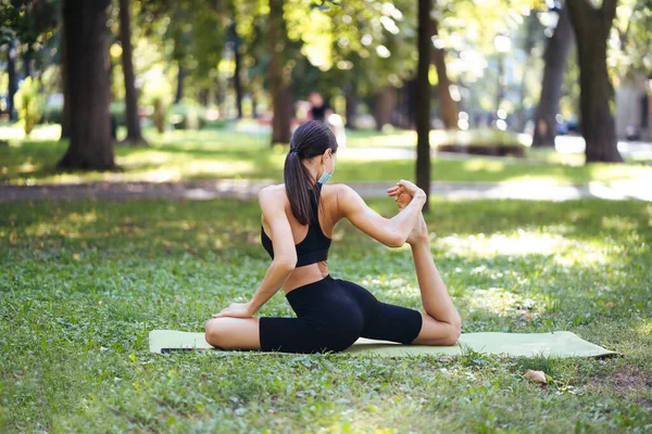 Sportliche junge Frau in medizinischer Schutzmaske beim Yoga im Park — Stockfoto