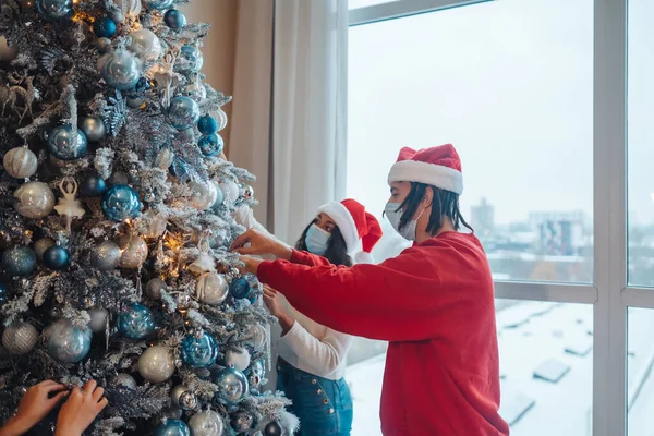 Seorang pemuda menghias pohon Natal dengan masker medis. — Stok Foto