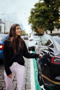 Elektrikli arabanın yanındaki kadın. Araç şarj istasyonunda yüklendi..