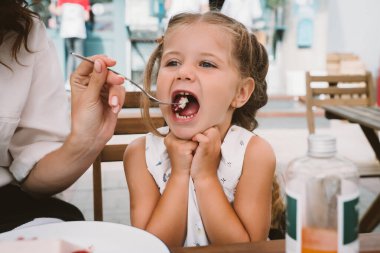 Genç anne sokakta gülümseyen çocukla pasta yiyor.