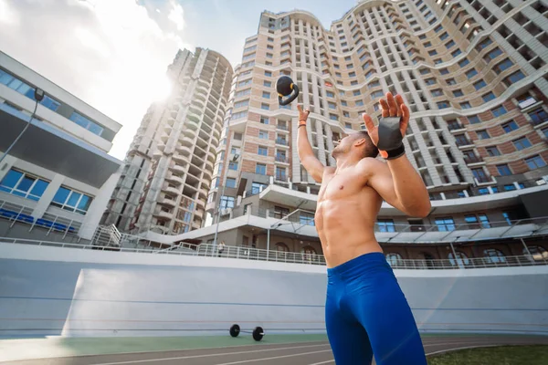 Treinamento esportivo cara com kettlebell no fundo de um prédio alto. Fotos De Bancos De Imagens