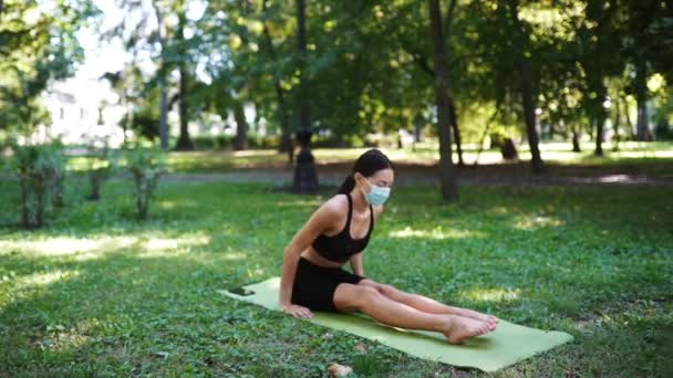 Sportos fiatal nő orvosi védőmaszkban, jógázik a parkban — Stock videók