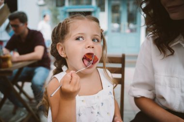 Genç anne sokakta gülümseyen çocukla pasta yiyor.