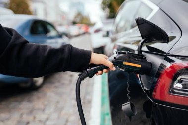 Elektrikli arabanın yanındaki kadın. Araç şarj istasyonunda yüklendi..