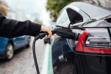 Elektrikli arabanın yanındaki kadın. Araç şarj istasyonunda yüklendi..