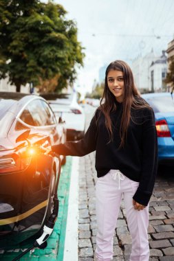 Elektrikli arabanın yanındaki kadın. Araç şarj istasyonunda yüklendi..
