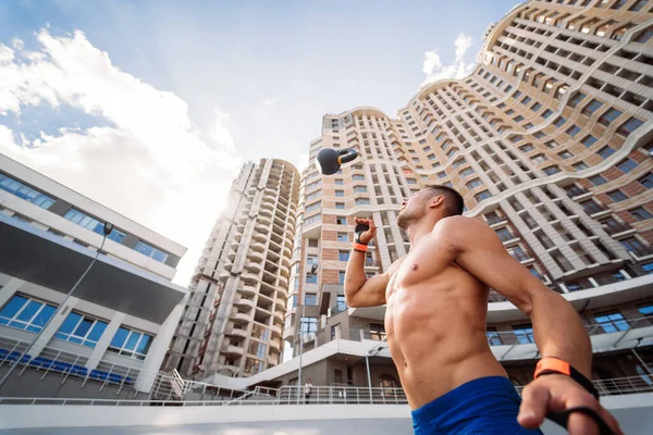Sportive guy training with kettlebell on the background of a tall building. Stock Picture