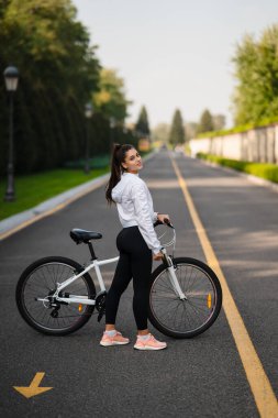 Beyaz bisiklete poz veren güzel bir kız. Doğada yürü.