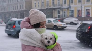 Kollarında köpek olan bir kız, kar yağıyor.