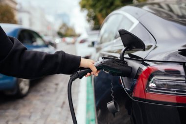 Elektrikli arabanın yanındaki kadın. Araç şarj istasyonunda yüklendi..