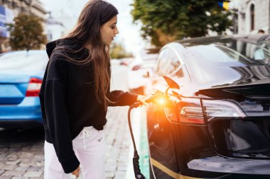 Elektrikli arabanın yanındaki kadın. Araç şarj istasyonunda yüklendi..