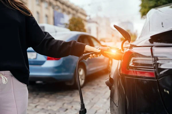 Mulher perto do carro eléctrico. Veículo carregado na estação de carregamento. — Fotografia de Stock