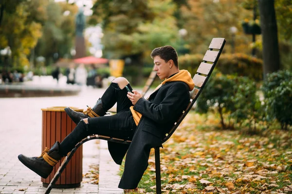 Young man sitting on a bench in park and listening to music — Stock Photo, Image