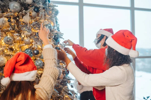 Unge mennesker pynter juletreet med medisinske masker. – stockfoto