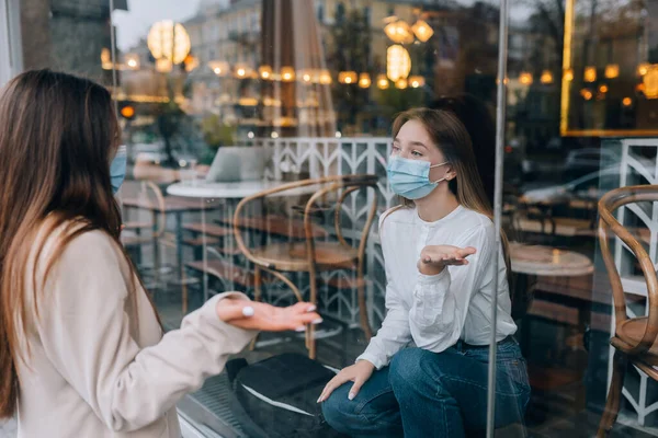 Dos mujeres con máscaras protectoras una frente a la otra, ventana entre ellas. —  Fotos de Stock