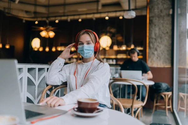Egy lány ül egy kávézóban fejhallgatóval. Coronavirus-járvány. — Stock Fotó