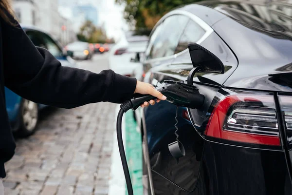 Egy nő az elektromos autó mellett. A töltőállomáson feltöltött jármű. — Stock Fotó