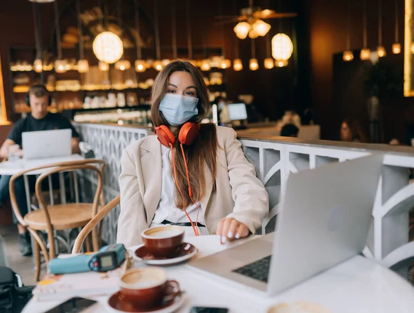 Девушка сидит в кофейне в наушниках. Вспышка коронавируса. — стоковое фото