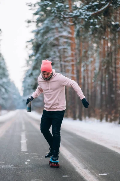 Skateboarder de pé na estrada no meio da floresta, cercado por neve — Fotografia de Stock