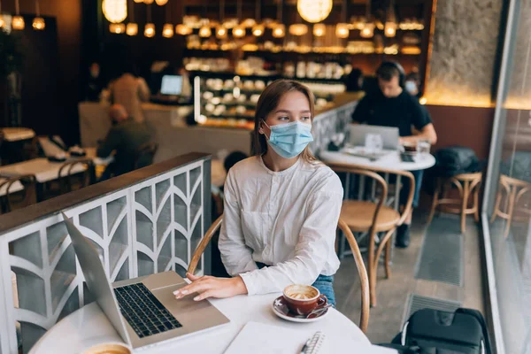 Hezká žena v lékařské masce obličeje, pomocí notebooku do práce. — Stock fotografie