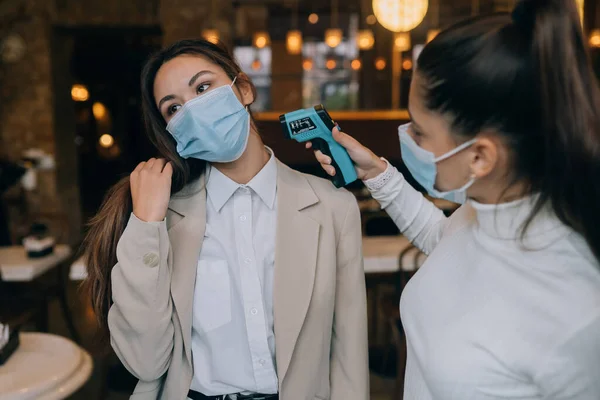 Woman measuring body temperature with contactless body thermometer