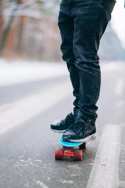 Skateboarder debout sur la route au milieu de la forêt, entouré de neige — Photo