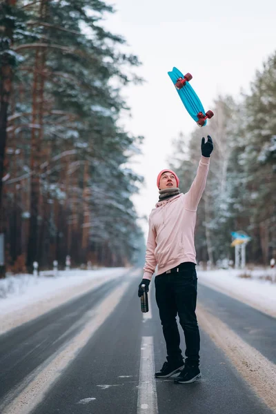 Skateboarder de pé na estrada no meio da floresta, cercado por neve — Fotografia de Stock