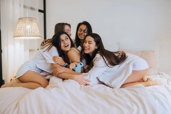 Positivo meninas mulheres amigas dentro de casa na cama na festa das galinhas em casa. — Fotografia de Stock