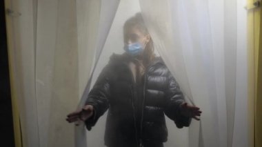 Koruyucu maskeli bir kız dezenfeksiyon odasından çıkıyor.