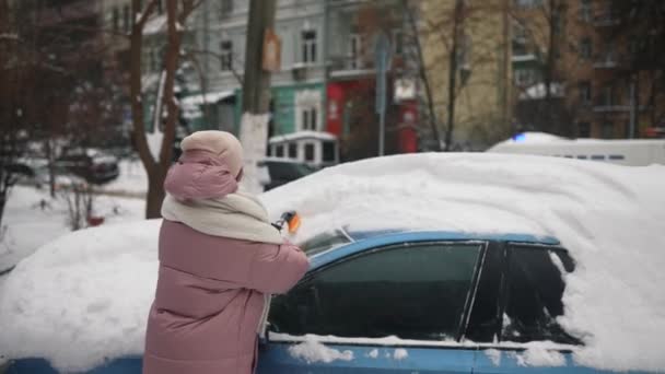 Женщина убирает снег из машины — стоковое видео