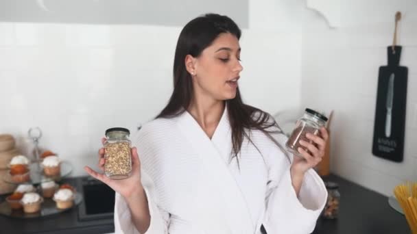 Hermosa chica sonriente vestida con albornoz blanco preparando el desayuno. — Vídeos de Stock