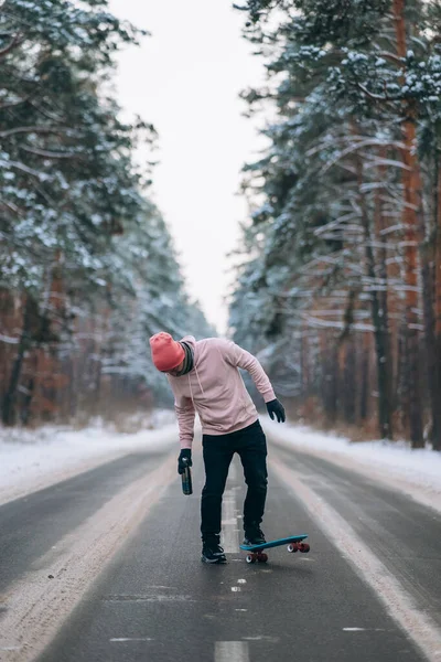 Skateboarder de pé na estrada no meio da floresta, cercado por neve — Fotografia de Stock