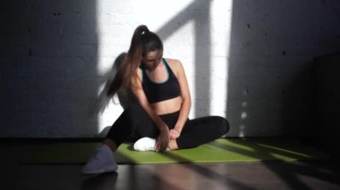 Formda bir kadın antrenmandan sonra dinleniyor, paspasın üzerinde oturuyor.