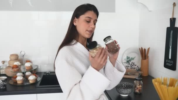 Menina sorridente bonita vestida com roupão branco preparando café da manhã. — Vídeo de Stock