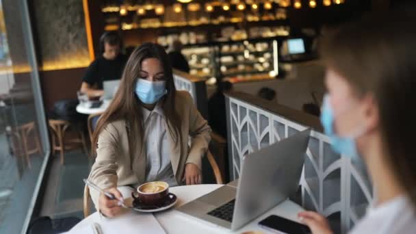 Zwei hübsche Frauen mit medizinischer Gesichtsmaske, die mit Laptop arbeiten. — Stockvideo