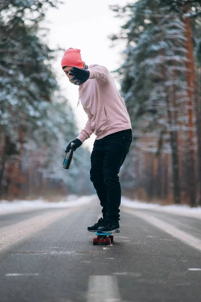 Skateboarder debout sur la route au milieu de la forêt, entouré de neige — Photo