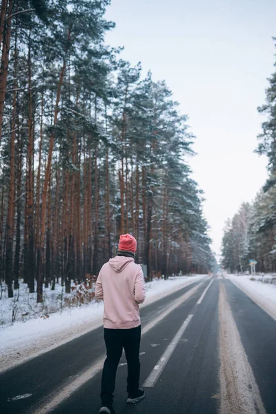 Хлопець стоїть на дорозі посеред лісу, оточений снігом — стокове фото