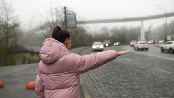 Молодая женщина, стоящая на улице, поднимая руку в сторону, ловит такси — стоковое видео