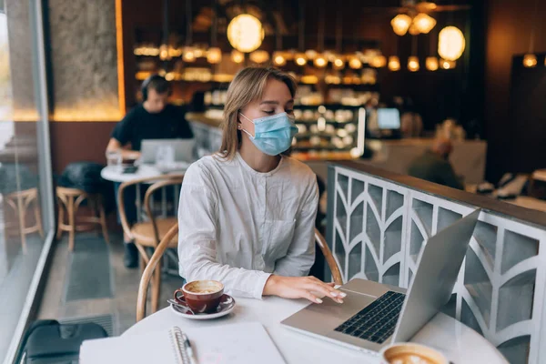 Красивая женщина в медицинской маске, использует ноутбук для работы. — стоковое фото