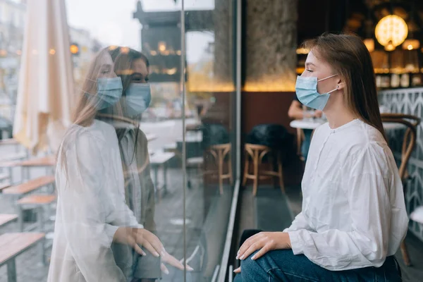 Две женщины в защитных масках напротив друг друга, окно между ними. — стоковое фото