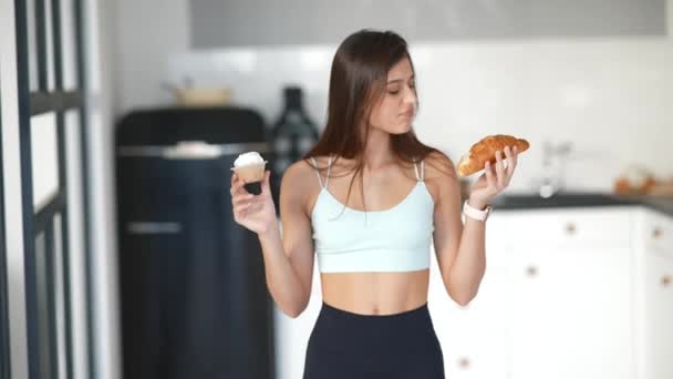 Una joven sostiene un croissant y un pastel en sus manos. — Vídeo de stock
