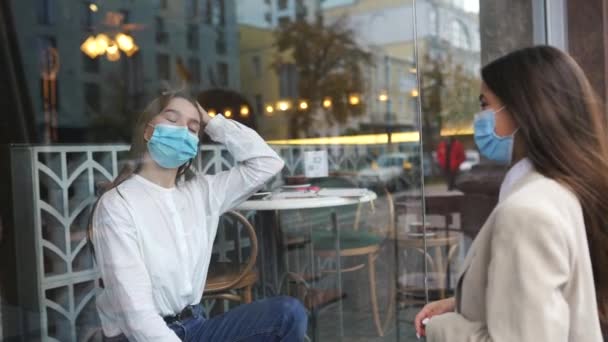 Dvě ženy v ochranných maskách naproti sobě, okno mezi nimi. — Stock video