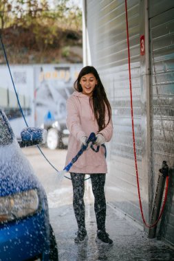 Yüksek basınçlı bir hortumdan esmer bir kadın arabaya temizlikçi yerleştirir.
