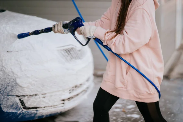 Yüksek basınçlı bir hortumdan esmer bir kadın arabaya temizlikçi yerleştirir. — Stok fotoğraf